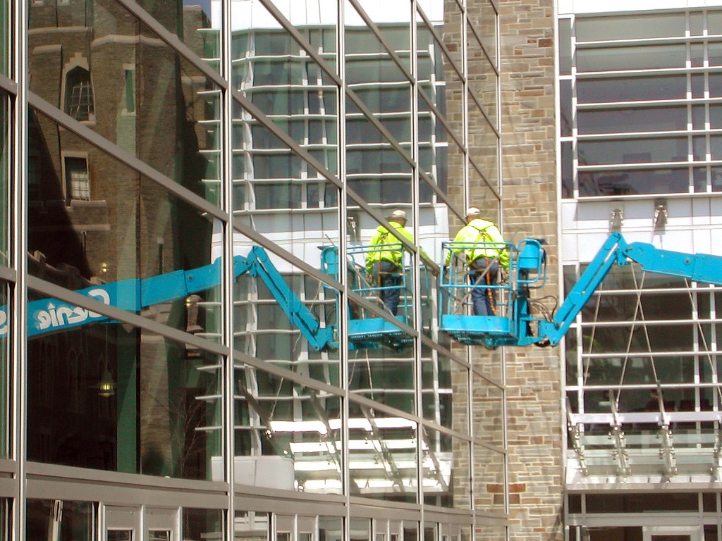 Two commercial window cleaners on cherry-picker lifts washing a glass office facade — commercial window cleaning