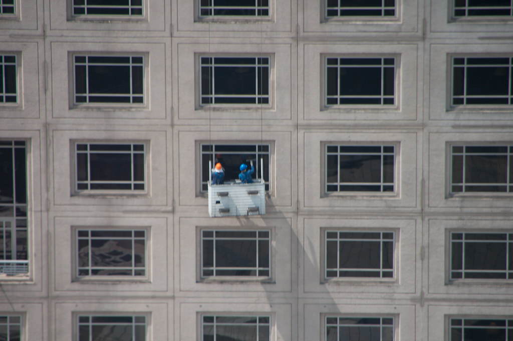 Two window cleaners on a suspended cradle washing high-rise office windows — commercial and high-reach window cleaning