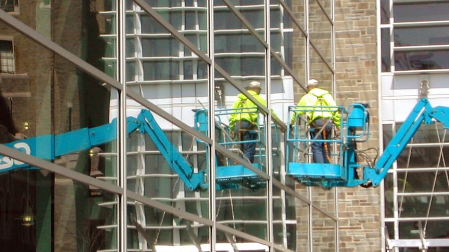Two commercial window cleaners on cherry-picker lifts washing a glass office facade — commercial window cleaning