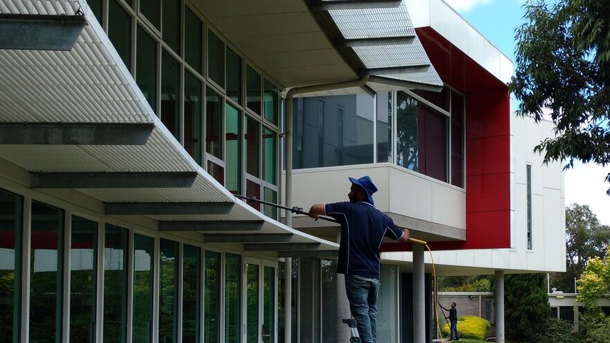 Window cleaner using a water-fed pole on upper-storey windows of a modern building — water-fed pole window cleaning